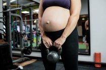 Femme enceinte levant cloche bouilloire dans la salle de gym — Photo de stock
