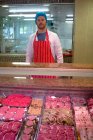 Retrato del carnicero parado en el mostrador de carne en la carnicería - foto de stock