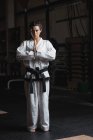 Retrato de mujer en kimono de karate de pie con las manos en gesto namaste en el gimnasio - foto de stock