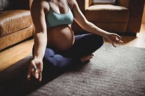 Imagen recortada de la mujer embarazada realizando yoga en la sala de estar en casa - foto de stock