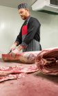 Carnicero cortando las costillas de la canal de cerdo en la carnicería - foto de stock