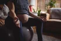 Обрезанный образ беременной женщины, занимающейся йогой на фитнес-мяч в гостиной на дому — стоковое фото