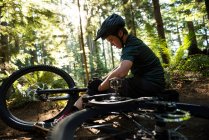 Мужчина-велосипедист чинит свой велосипед в лесу в солнечный день — стоковое фото