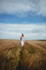 Mulher bonita caminhando através do campo de trigo no dia ensolarado — Fotografia de Stock