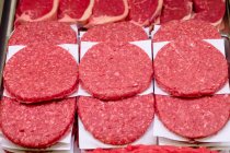 Close-up of raw hamburger patties on paper on display — Stock Photo