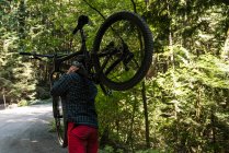 Cycliste homme portant le vélo de montagne tout en marchant dans le parc — Photo de stock