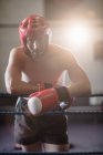 Male boxer in protective boxing helmet leaning on ropes of boxing ring at fitness studio — Stock Photo