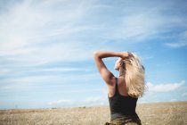 Вид сзади на блондинку, стоящую в поле с руками в волосах — стоковое фото