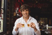 Portrait of bartender holding whisky shot glasses at bar counter in bar — Stock Photo