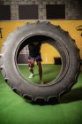 Strong sportsman lifting heavy tire in gym — Stock Photo