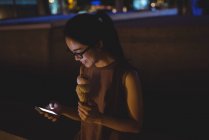 Young woman using mobile phone while having ice-cream at night — Stock Photo