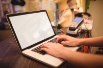 Mains de personnel féminin utilisant un ordinateur portable à un comptoir dans un magasin de boutique — Photo de stock