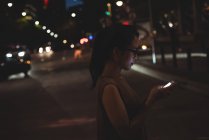 Giovane donna che utilizza il telefono cellulare in strada di notte — Foto stock