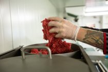Primer plano de la mano del carnicero poniendo carne en la máquina picadora - foto de stock