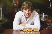 Portrait of bartender with tray of whisky shot glasses at bar counter in bar — Stock Photo