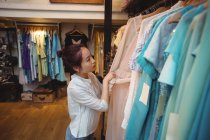Mulher selecionando roupas em cabides na loja de roupas — Fotografia de Stock