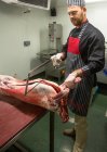 Мясник режет тушу свинины пилой в мясной лавке — стоковое фото