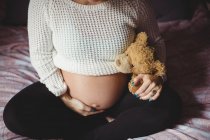 Imagem cortada de mulher grávida segurando ursinho de pelúcia no quarto em casa — Fotografia de Stock