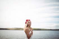 Lächelnde blonde Frau im Blume-Diadem, die am Fluss steht — Stockfoto