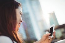 Mensajería de texto de mujer joven en el teléfono móvil en la ciudad - foto de stock