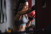 Portrait de boxeuse pratiquant la boxe avec sac de boxe dans un studio de fitness — Photo de stock