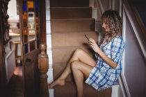 Bella donna seduta sulle scale e utilizzando il telefono cellulare a casa — Foto stock
