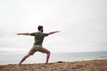 Vista trasera del hombre realizando ejercicio de estiramiento en la playa - foto de stock