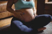Imagen recortada de la mujer embarazada relajante y tocando el vientre en la sala de estar - foto de stock