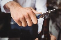 Крупный план бармена, открывающего бутылку пива у барной стойки — стоковое фото
