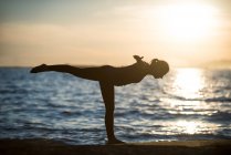 Vista lateral da mulher realizando ioga na praia durante o pôr do sol — Fotografia de Stock