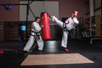 Vista lateral de hombre y mujer practicando karate con saco de boxeo en estudio - foto de stock