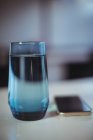 Vaso de agua y teléfono móvil sobre mesa en oficina - foto de stock