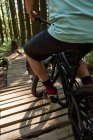 Обрезанный вид велосипедиста мужского пола, катающегося на велосипеде в лесу при солнечном свете — стоковое фото