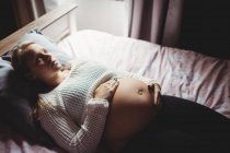 Vue grand angle de femme enceinte réfléchie se détendre dans la chambre à coucher à la maison — Photo de stock