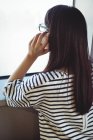 Вид ззаду жінки, що дивиться через вікно під час розмови на мобільному телефоні — стокове фото