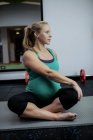 Pregnant woman performing stretching exercise on exercise mat in gym — Stock Photo