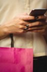 Seção média de mulher usando telefone celular enquanto faz compras na loja de boutique — Fotografia de Stock