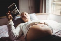 Enfoque selectivo de la mujer embarazada mirando la sonografía en el dormitorio en casa - foto de stock