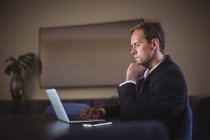 Pensativo hombre de negocios utilizando el ordenador portátil en el escritorio en la oficina - foto de stock
