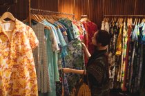Жінка вибирає одяг на вішалках в магазині одягу — стокове фото