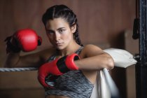 Tired boxer in boxing gloves leaning on ropes of boxing ring at fitness studio and looking at camera — Stock Photo