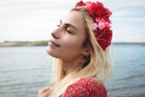 Portrait of blonde woman in flower wreath standing with closed eyes near river — Stock Photo