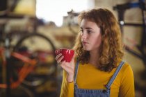 Задумчивая женщина, выпившая чашку кофе в магазине велосипедов — стоковое фото