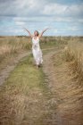 Carefree blonde woman standing on field path with raised arms — Stock Photo