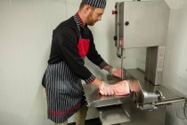 Butcher cutting pork in machine at butchers shop — Stock Photo