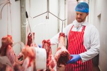 Açougueiro pendurado carne vermelha na sala de armazenamento no açougue — Fotografia de Stock