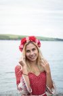 Retrato de mujer rubia sonriente en tiara de flores de pie cerca del río - foto de stock