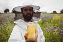 Apicoltore in possesso di bottiglia di miele in campo — Foto stock
