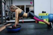 Femme faisant push-up sur boule de bosu dans la salle de gym — Photo de stock