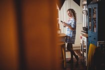 Mulher bonita usando telefone celular na cozinha em casa — Fotografia de Stock